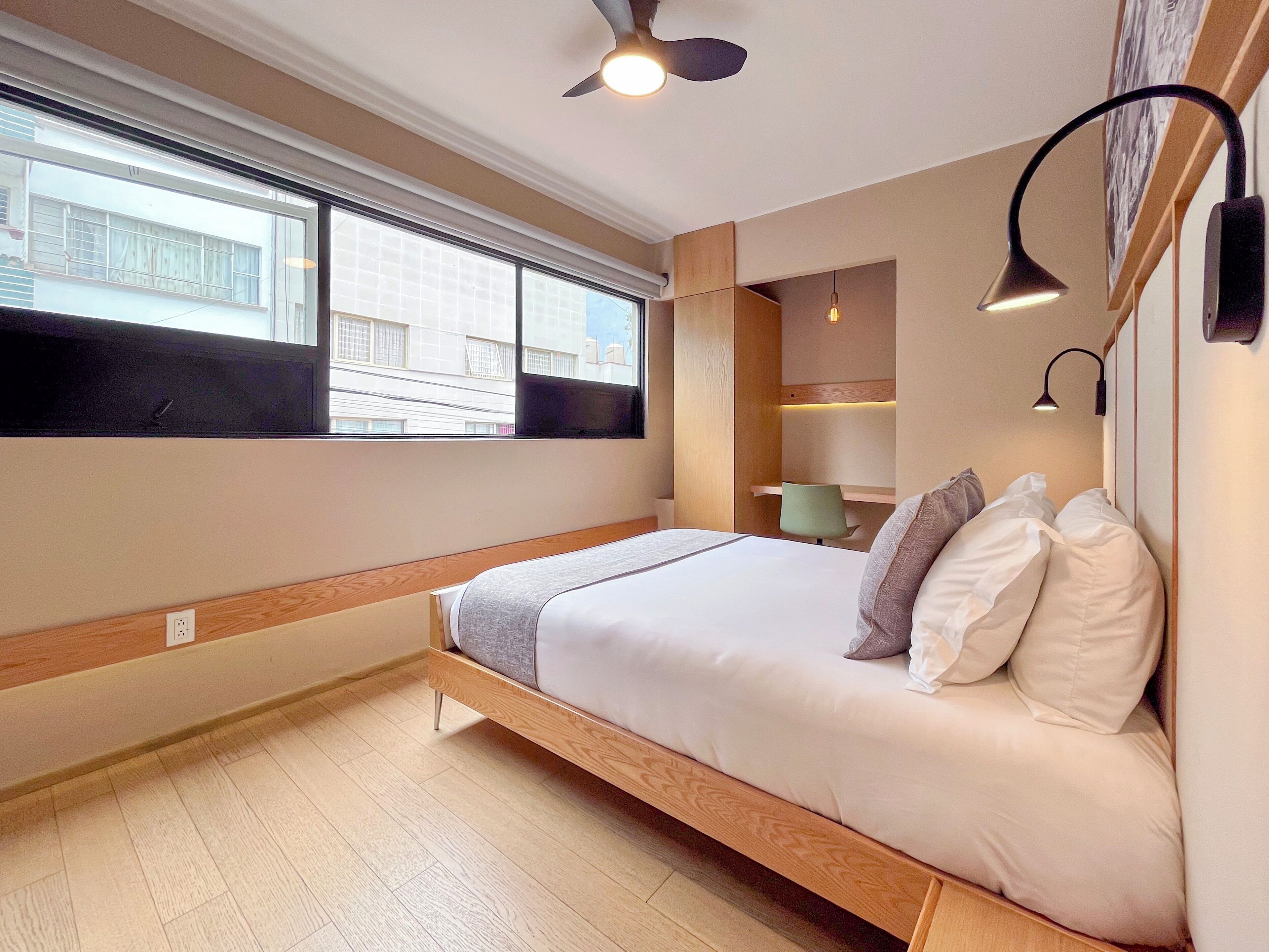 A modern bedroom with a wooden bed, a large window, and a ceiling fan.