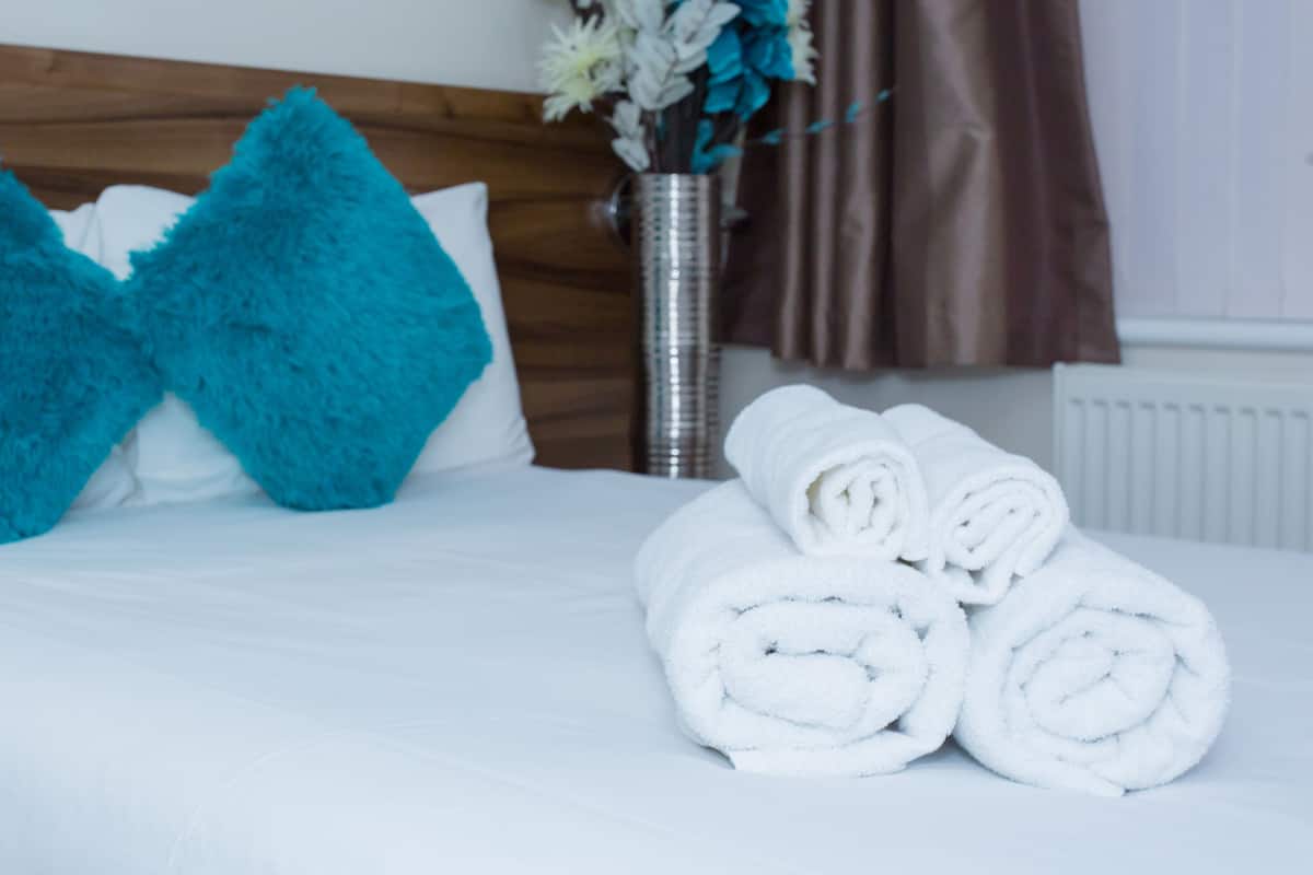 A neatly made bed with white bedding, two bright blue pillows, and a vase with flowers.