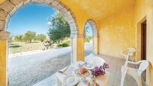Un coin repas avec une table dressée pour deux personnes, une vue sur un paysage rural et un bâtiment aux murs jaunes orné d’arches en pierre.