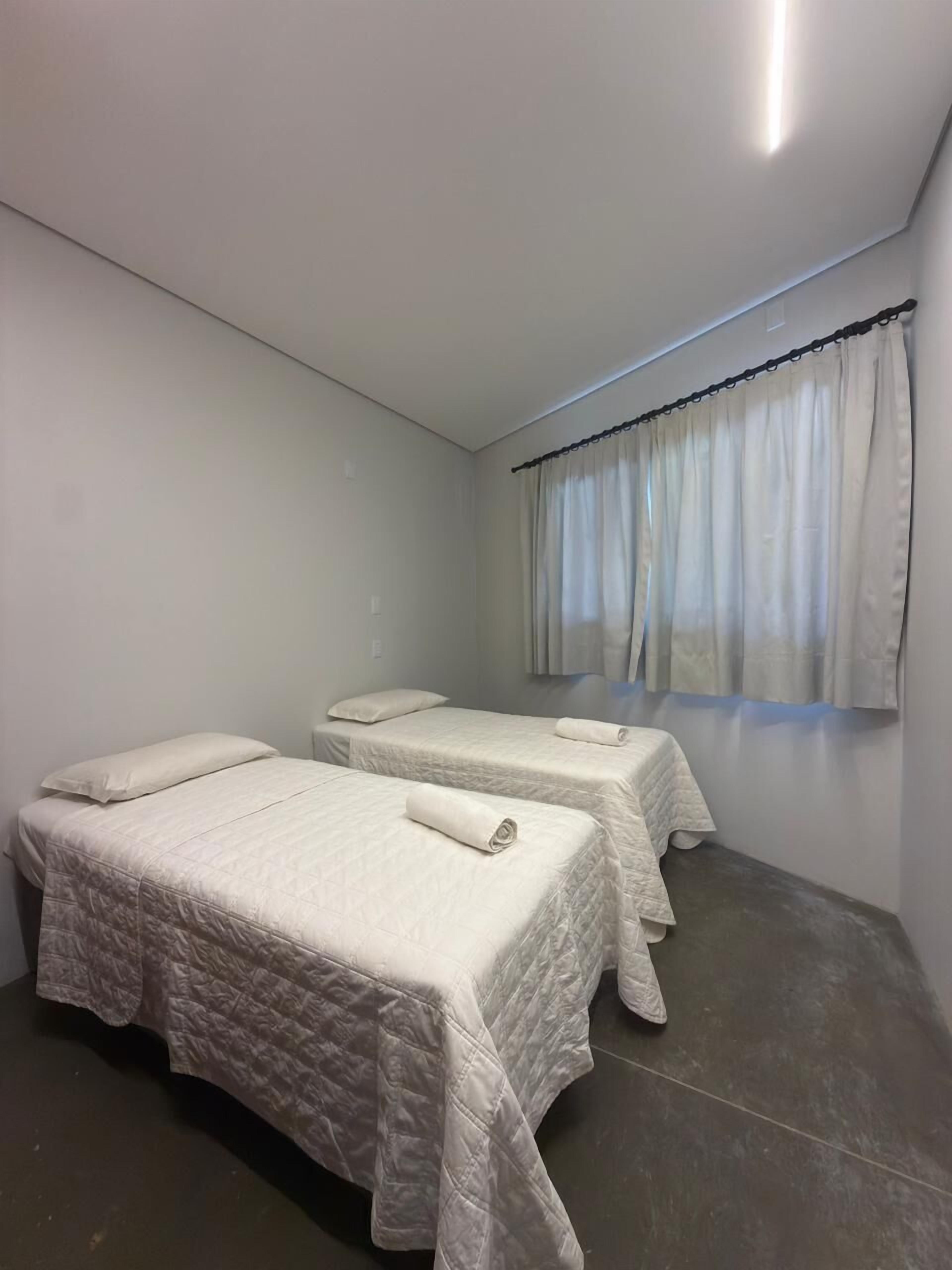 A room with two beds, a window with curtains, and a ceiling light.