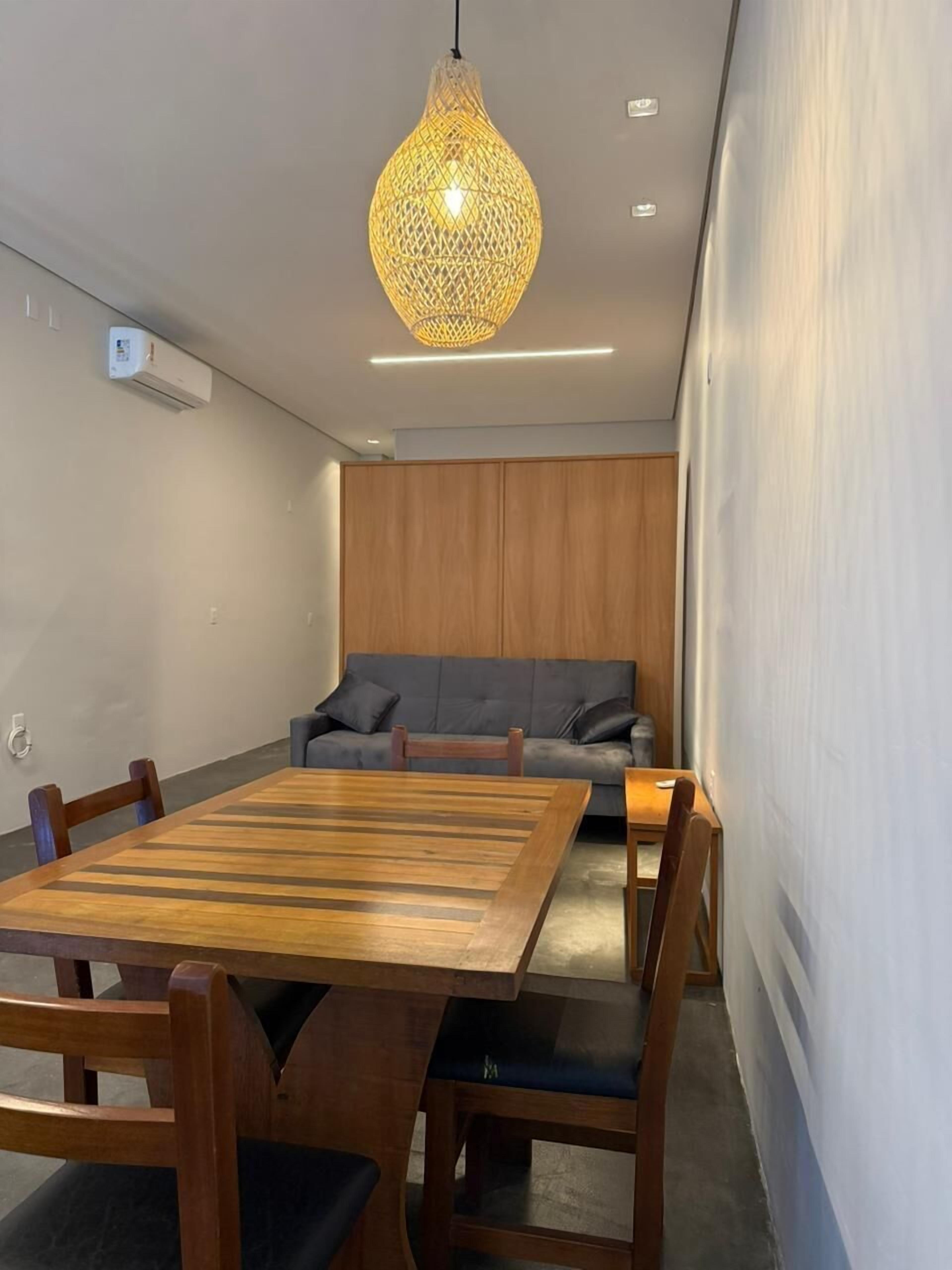 Una habitación moderna con una mesa de comedor de madera, sillas, un sofá gris y una lámpara colgante.