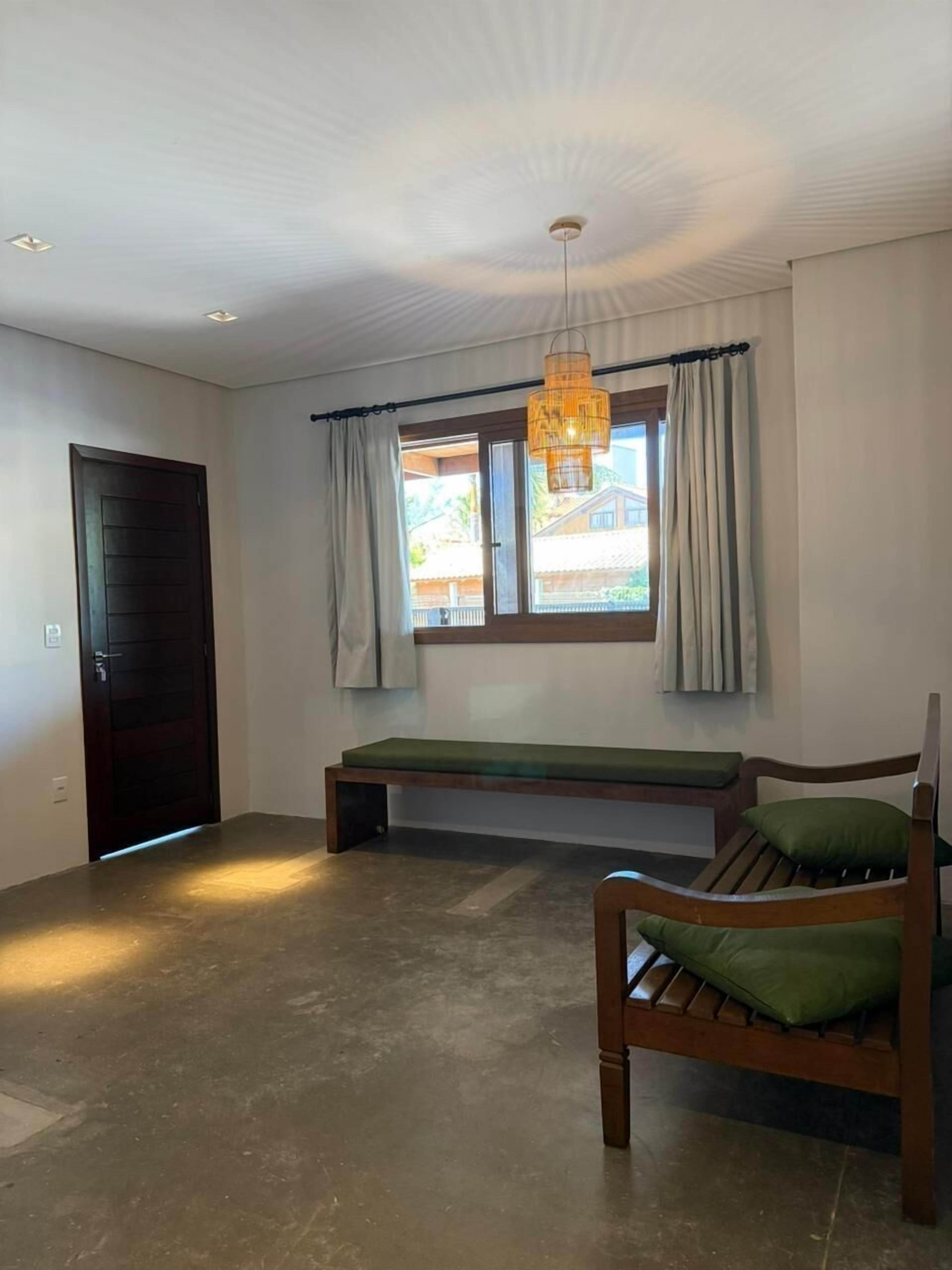 A room with a bench, a bed, a door, and a window with curtains.