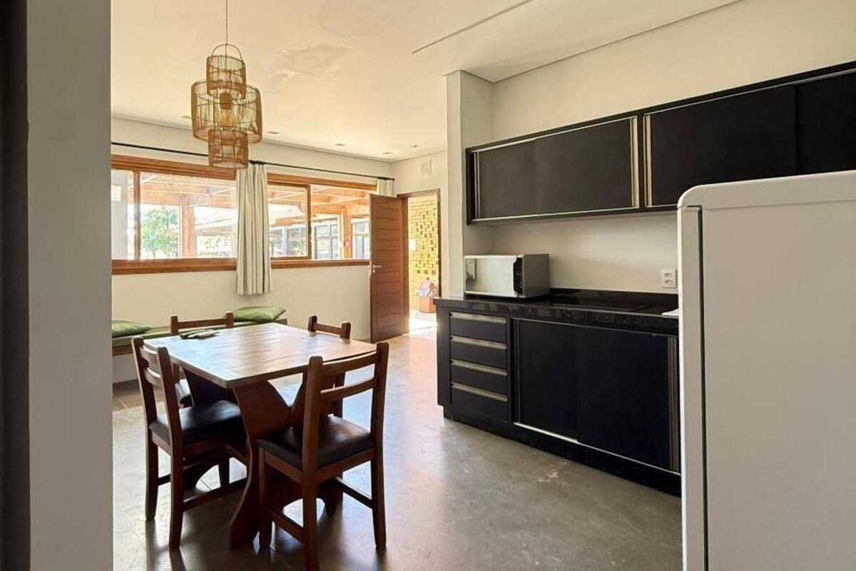 A modern kitchen with a dining area, large windows, and a hanging light fixture.