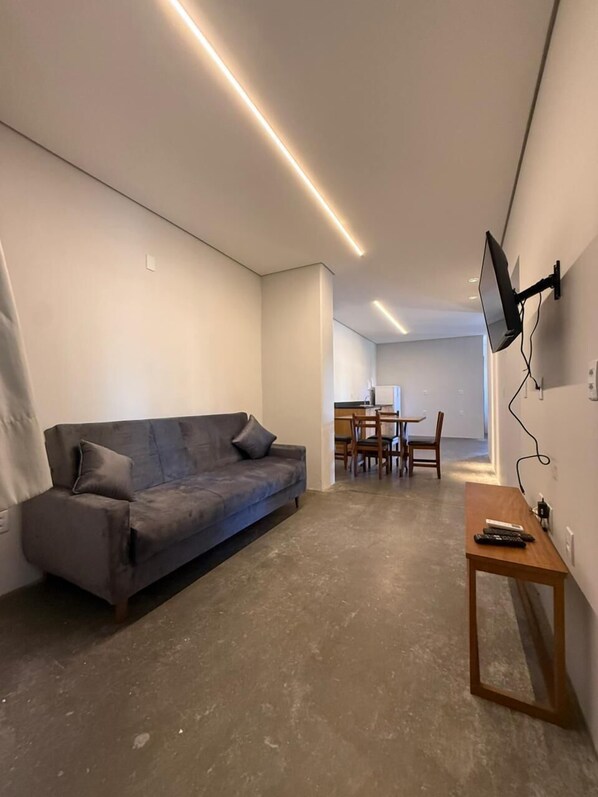 Una sala de estar moderna con un sofá gris, una mesa de centro de madera y un televisor montado en la pared.