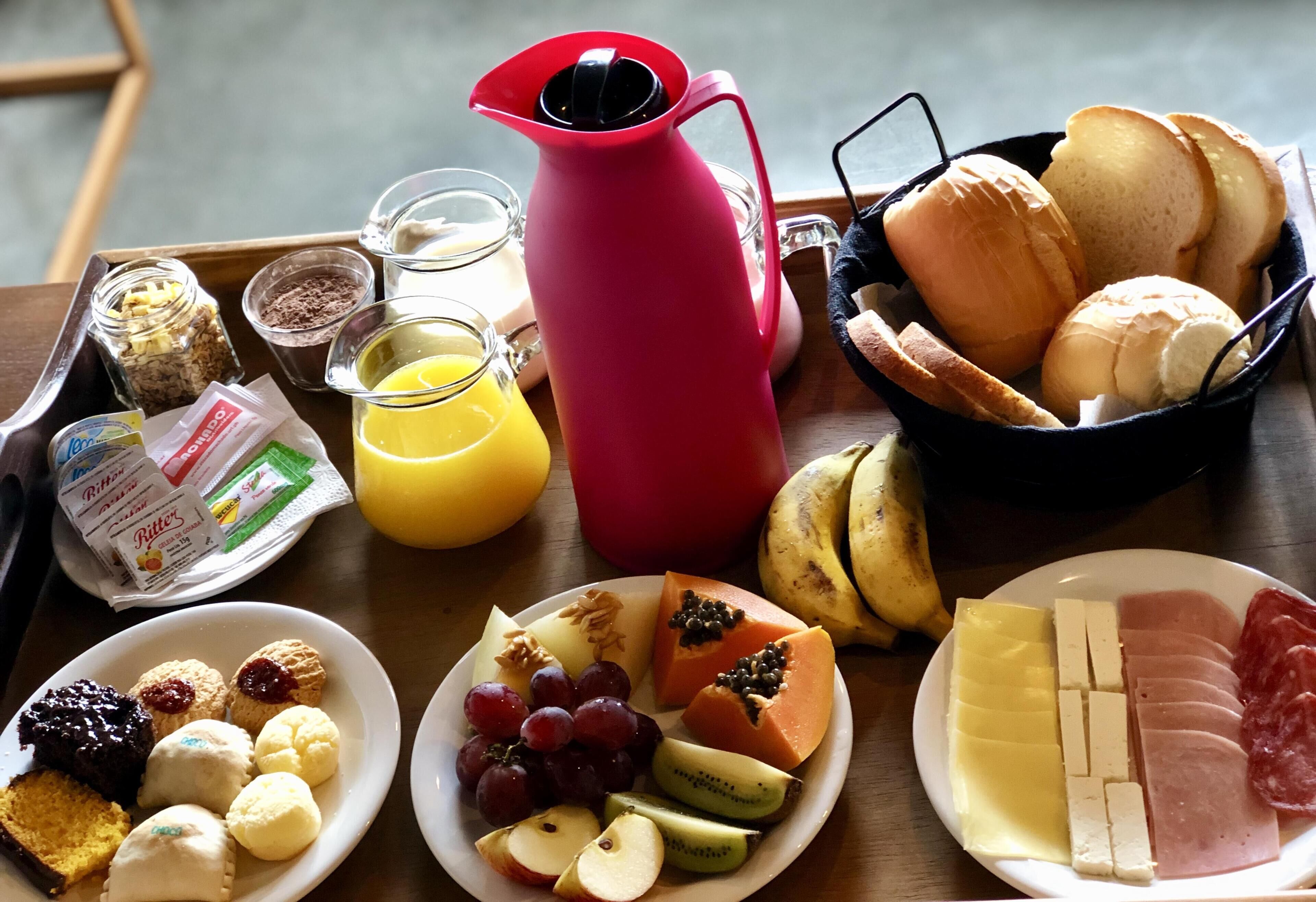 A breakfast tray with various foods, including bread, pastries, fruits, and cheese.