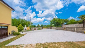 A residential driveway with a yellow house, gravel surface, and a clear blue sky with clouds. - Top vacation home with pool for 4+1 (Tinjan)