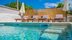 A pool area with lounge chairs and umbrellas, surrounded by a bamboo fence and a white wall. - Top vacation home with pool for 4+1 (Tinjan)
