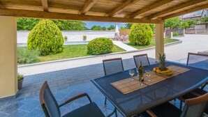 An outdoor patio with a table set for dining, surrounded by chairs, and overlooking a swimming pool and garden. - Top vacation home with pool for 4+1 (Tinjan)