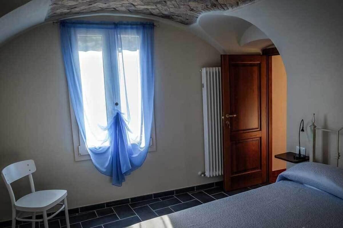 A room with a bed, a chair, a radiator, and a window with blue curtains.