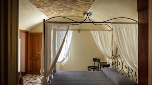 A bedroom with a four-poster bed, a wooden door, and a small table with a chair. - B&B U Campanin (Dolceacqua)