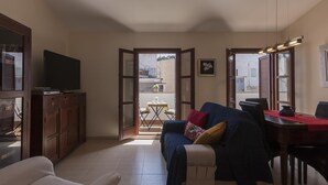 En stue med sofa, tv, spisebord og en balkon med bord og stole.