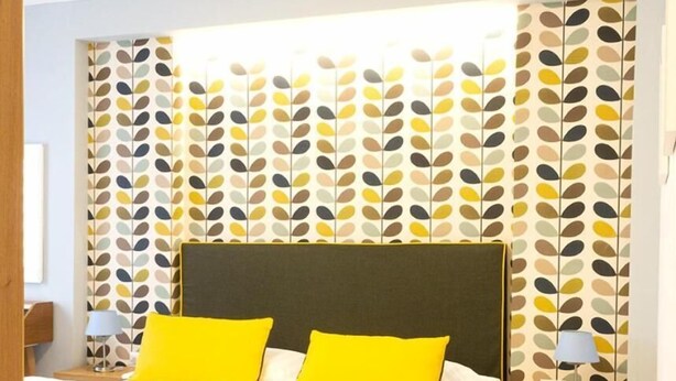 A neatly made bed with yellow pillows, a wooden headboard, and a patterned wallpaper. - B&B Veru' (Sorrento)