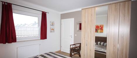 A bedroom with a bed, a chair, a wardrobe, and a window with curtains.
