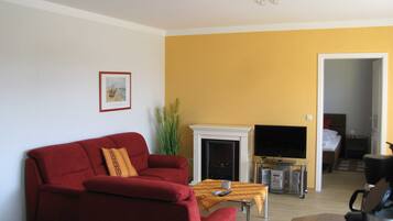 Una sala de estar con un sofá rojo, chimenea, televisor y cafetera.