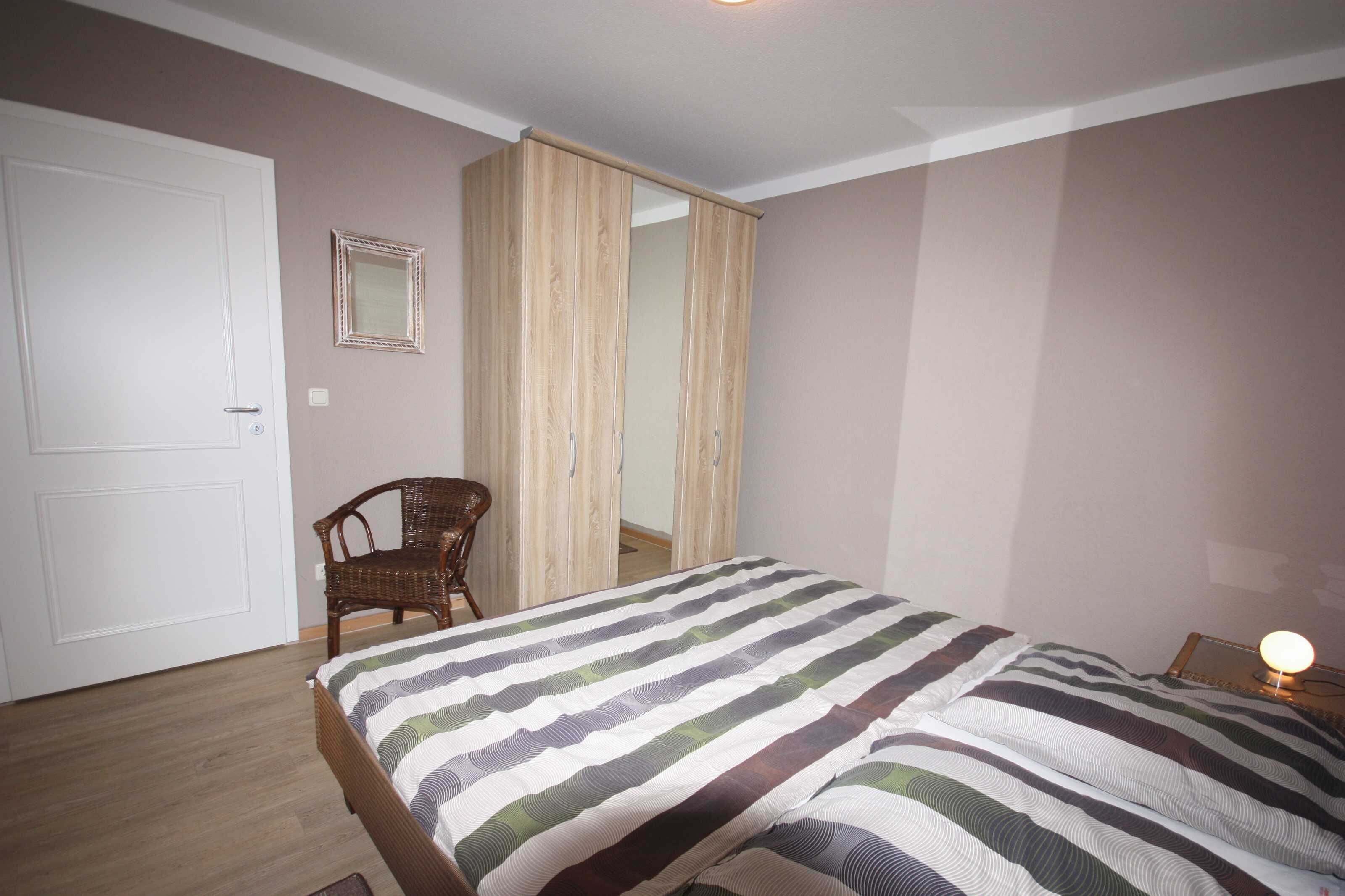 Un dormitorio con cama, una silla, un armario y una lámpara de noche.
