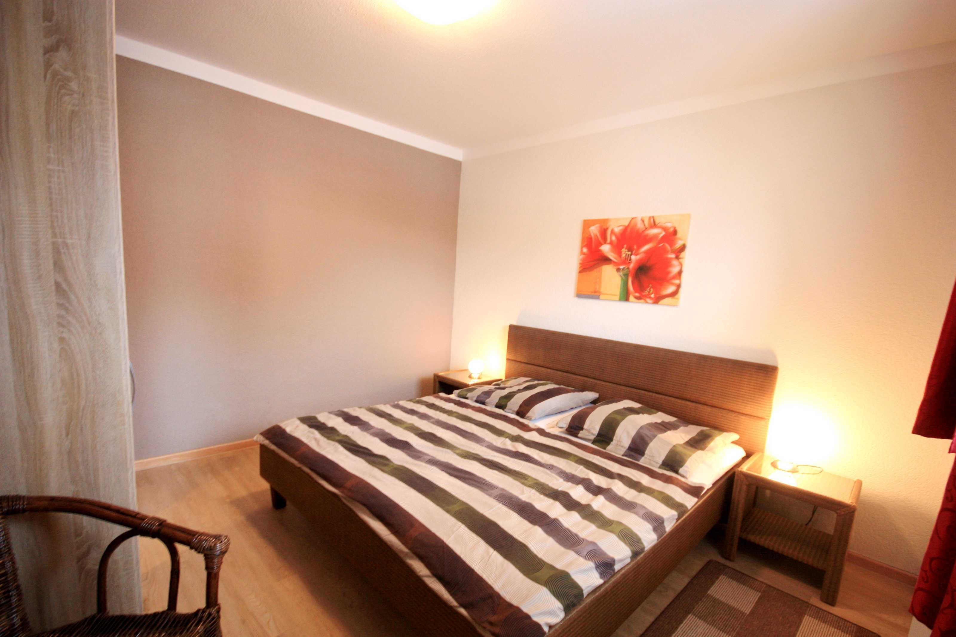 Une chambre à coucher comprenant un lit, deux tables de chevet, une chaise et une œuvre d’art accrochée au mur.