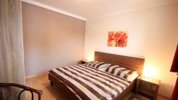 Une chambre à coucher comprenant un lit, deux tables de chevet, une chaise et une œuvre d’art accrochée au mur.