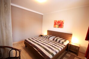 Une chambre à coucher comprenant un lit, deux tables de chevet, une chaise et une œuvre d’art accrochée au mur.