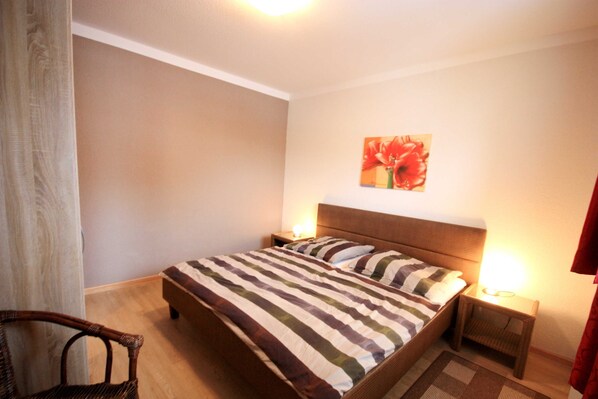 A bedroom with a bed, two bedside tables, a chair, and a wall-mounted artwork.