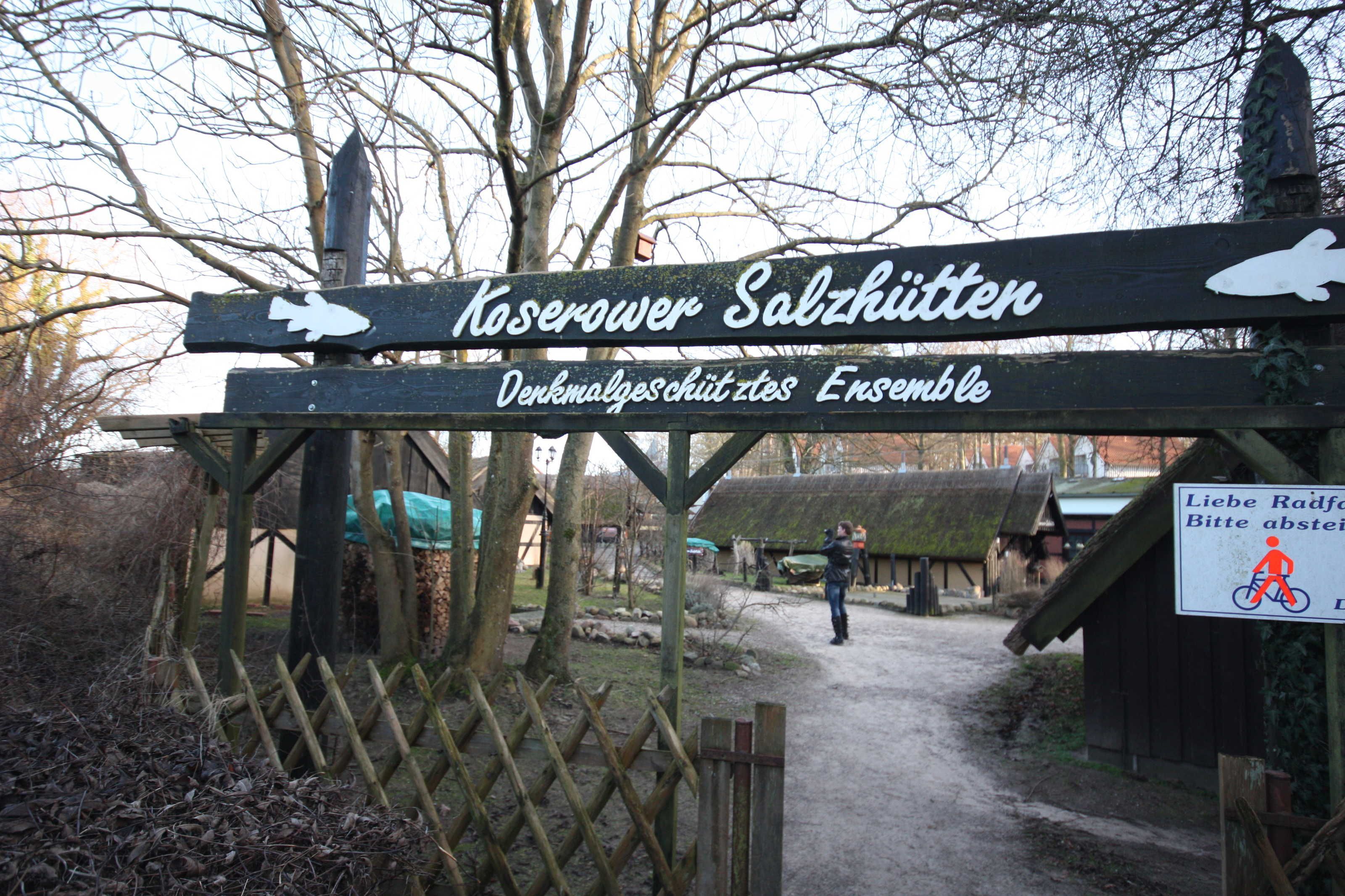 A wooden sign with text and a bicycle symbol, indicating a path or entrance to a location.