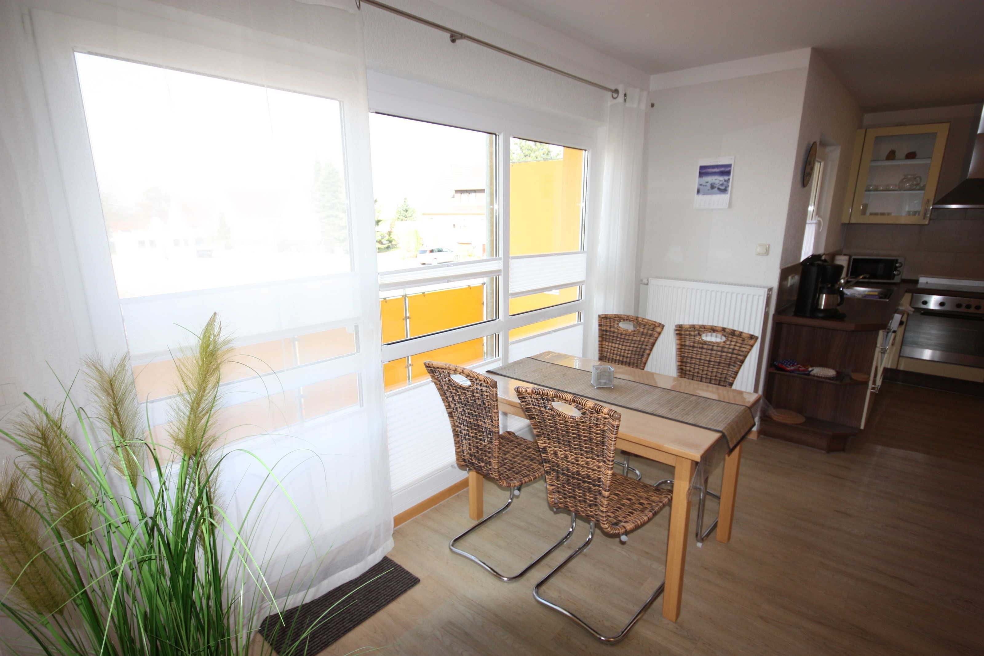Un espace repas avec une table et des chaises, une vue dégagée grâce à de grandes fenêtres, et une cuisine en arrière-plan.