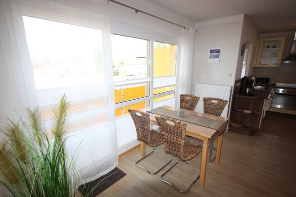 Un espace repas avec une table et des chaises, une vue dégagée grâce à de grandes fenêtres, et une cuisine en arrière-plan.