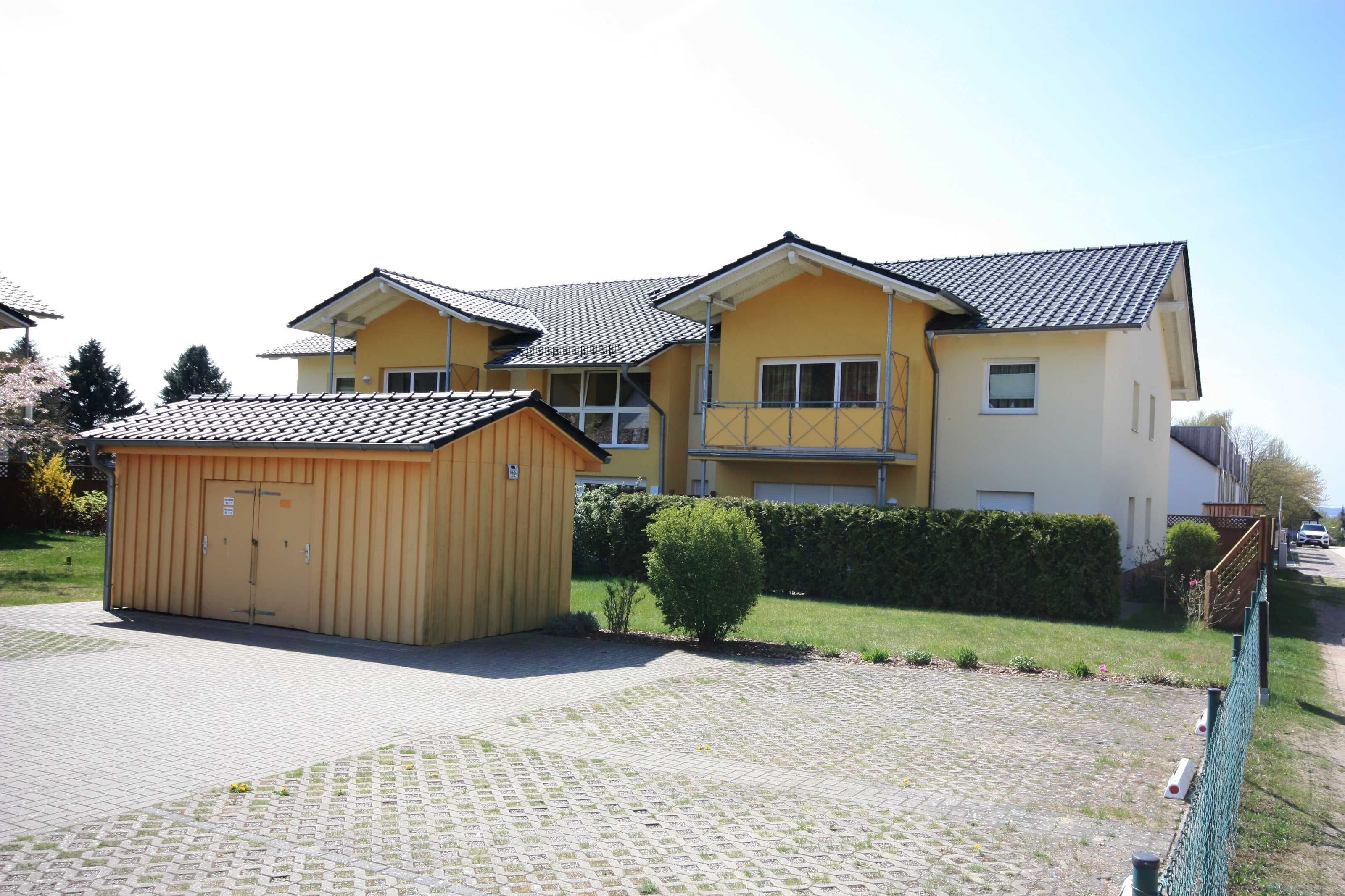 A two-story residential building with a garage, a small shed, and a paved driveway.