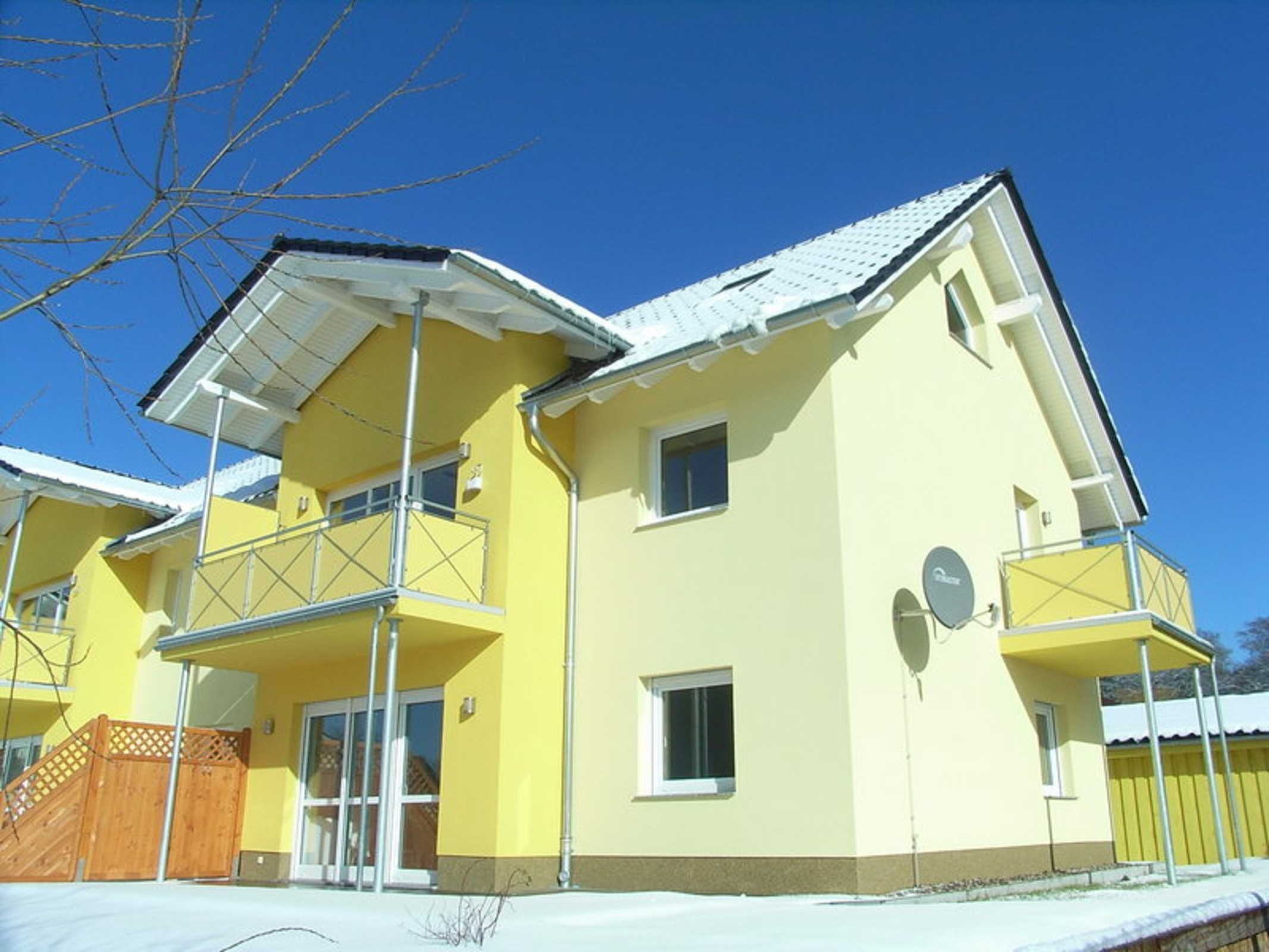 A two-story yellow building with a balcony, a satellite dish, and a wooden fence.