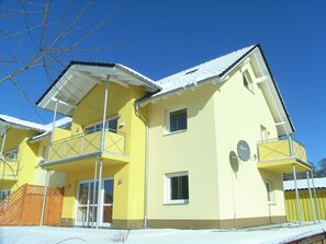 Un bâtiment jaune à deux étages, doté d’un balcon, d’une antenne parabolique et d’une clôture en bois.