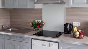 A modern kitchen with white cabinets, a stainless steel sink, a stove, and a dishwasher. There is a flower vase on the counter and a fruit basket. - Pretty Penty in the heart of Trégor (Pommerit-Jaudy)