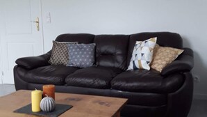 A living room with a dark leather sofa, a wooden coffee table, and a framed picture on the wall. - Pretty Penty in the heart of Trégor (Pommerit-Jaudy)