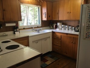 Una cocina compacta con armarios de madera, encimera blanca, estufa y refrigerador.