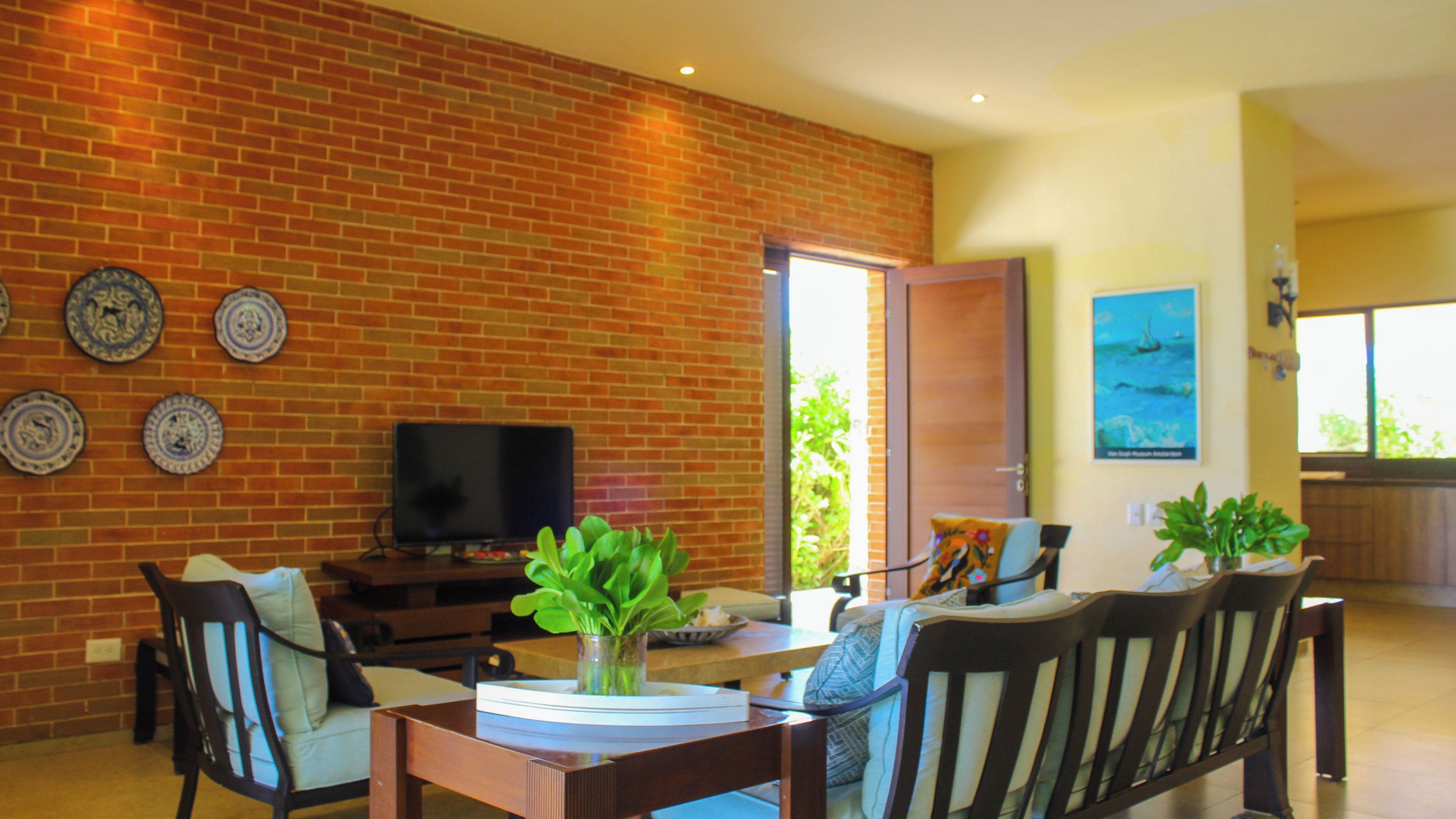 A living room with a brick wall, a television, and a dining area with chairs and a table.