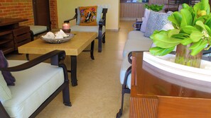A dining area with a wooden table, chairs, a bowl of seashells, a lit candle, and a sofa with patterned cushions.