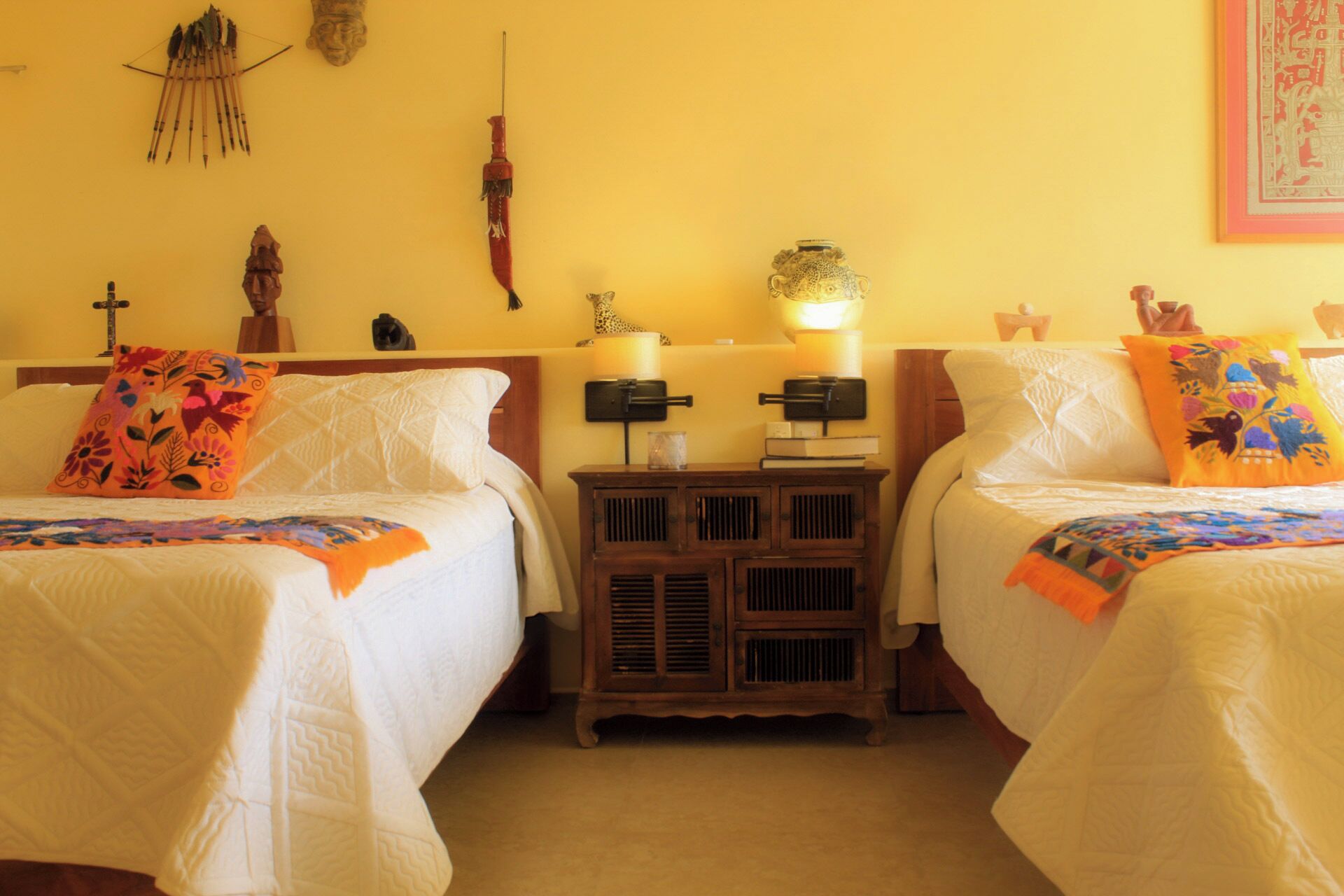 Twee bedden met witte lakens, een houten nachtkastje met twee lampen en een decoratief object aan de muur.