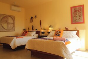A room with two beds, each with a white bedspread and multiple pillows, a nightstand with a lamp, and a wall with a framed picture and a decorative item.