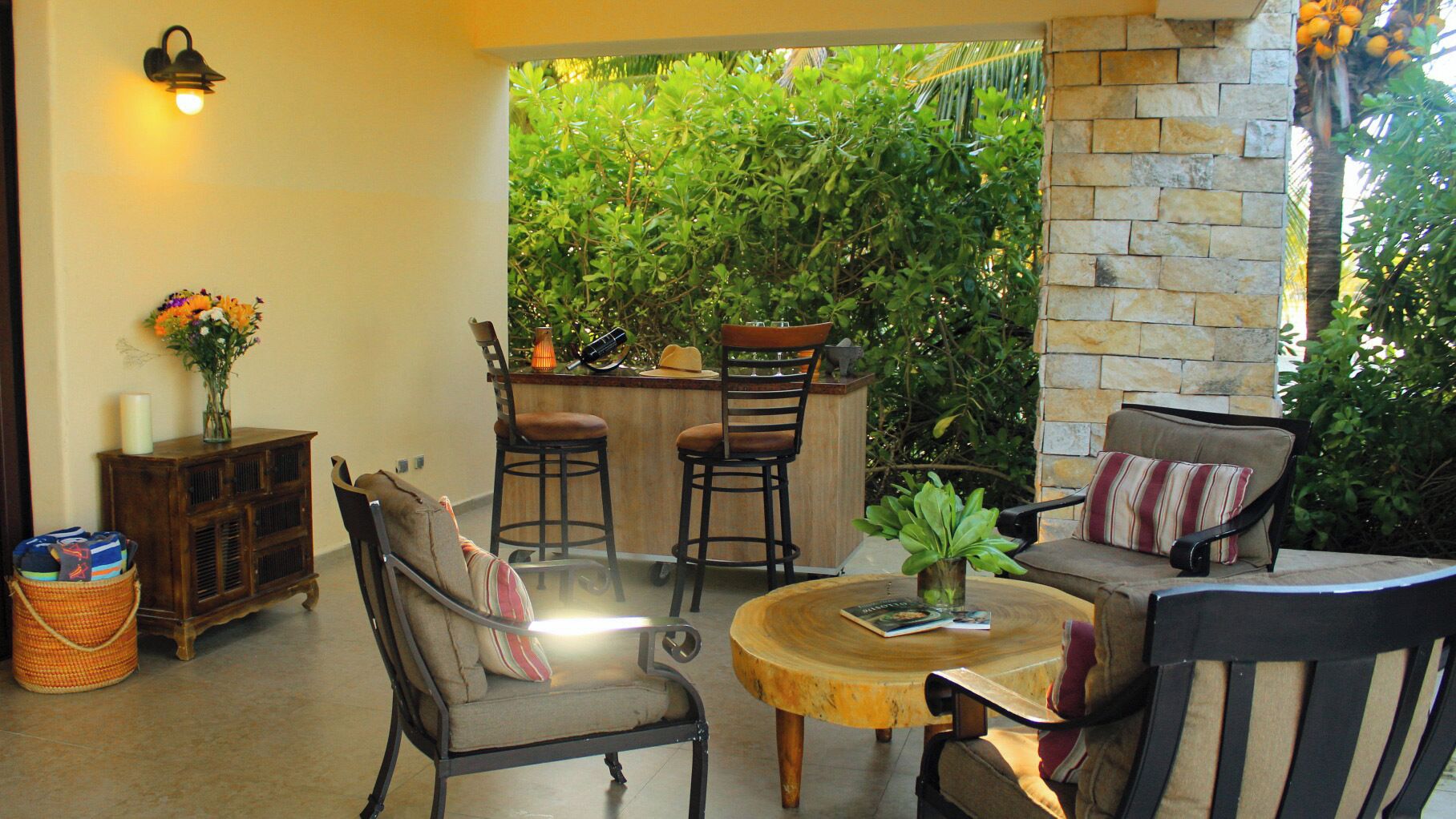 A cozy patio area with a stone wall, a wooden bar, and seating including a sofa and chairs.