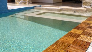 Une piscine aux eaux cristallines, bordée d’une terrasse en bois et dotée de marches en pierre menant à l’eau.