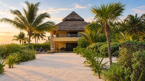 Resort com um prédio de telhado de palha, palmeiras e um caminho de areia que leva à entrada.