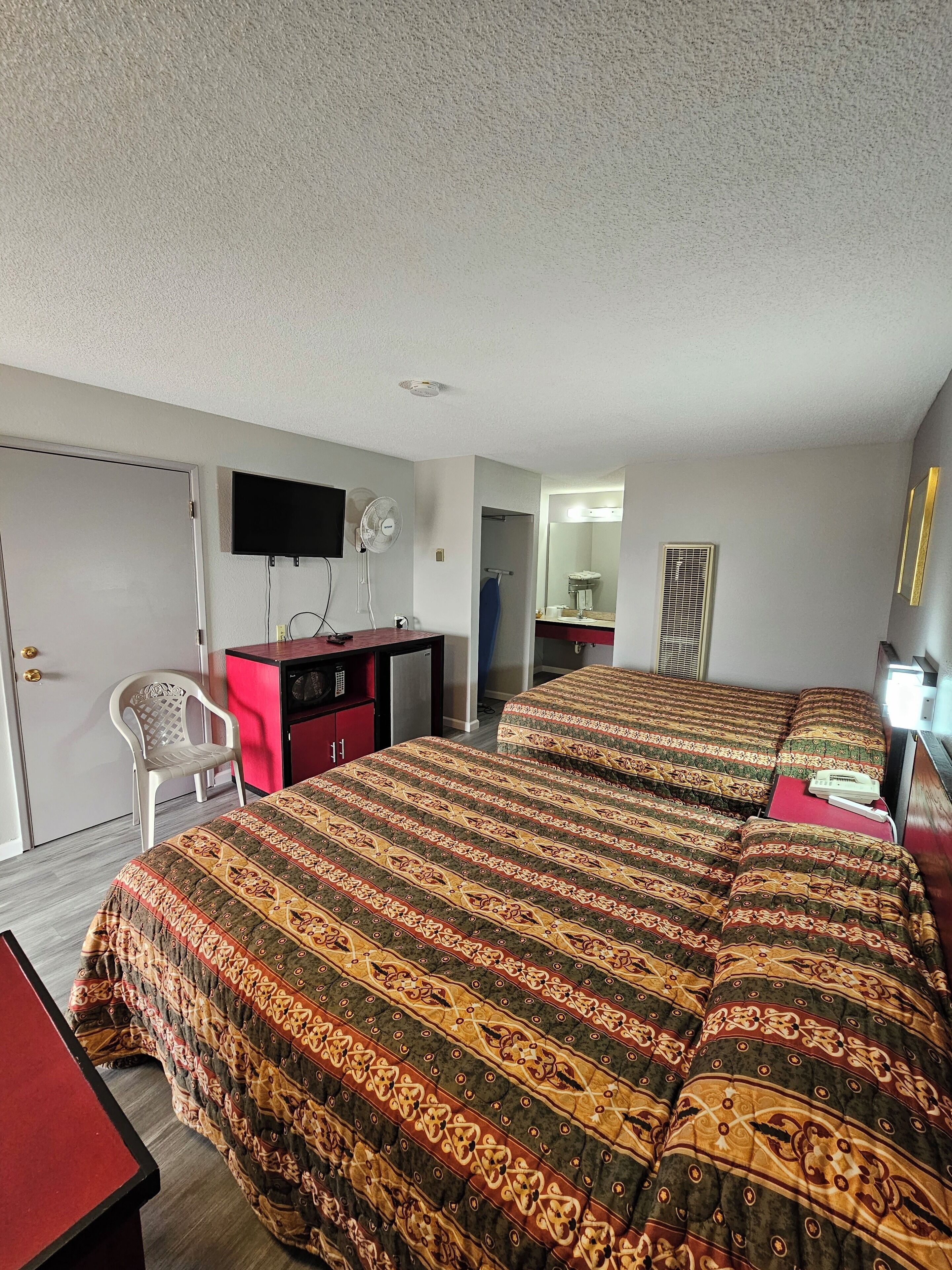A hotel room with two beds, a desk, a chair, a TV, and a bathroom visible through an open door.