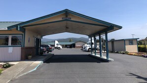 A parking area with a covered entrance, a clear sky, and a view of mountains in the distance. - Travel Inn (Fortuna)