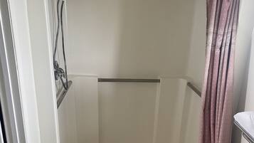 Een douche met een glazen deur, douchekop en douchegordijn.