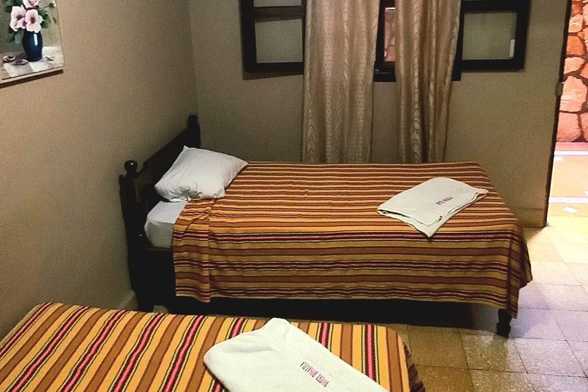 A hotel room with two beds, a window with curtains, a mirror, and a painting on the wall.