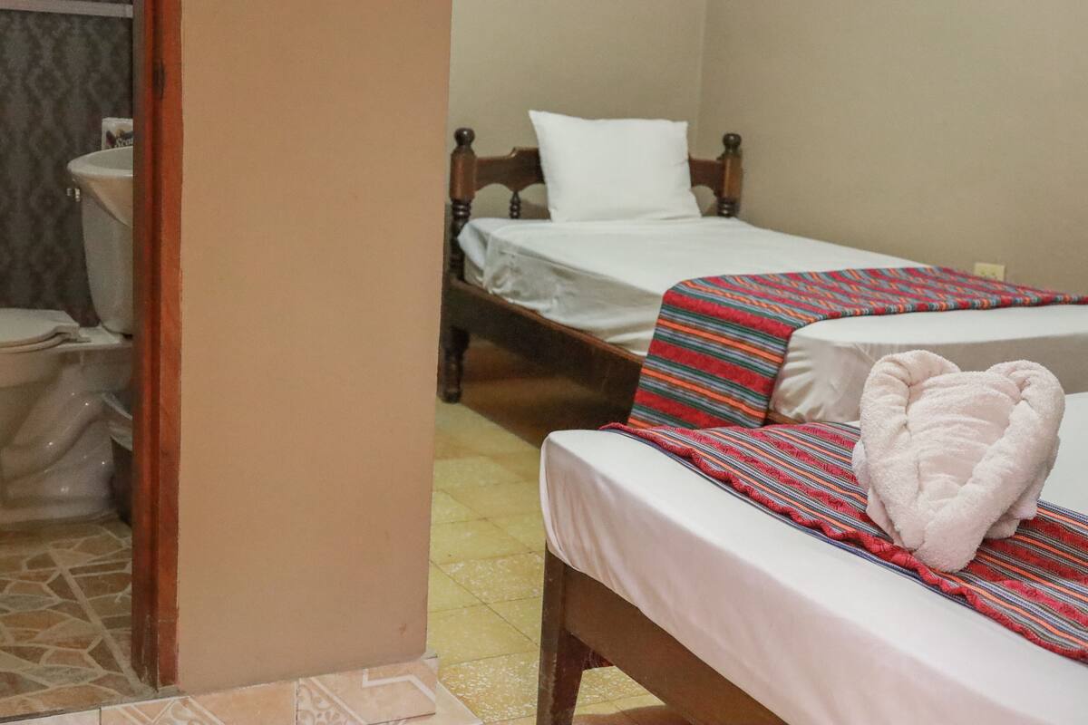 A room with two beds, a wooden headboard, a white pillow, a striped bedspread, and a white towel on the bed.