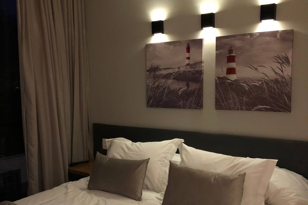 A hotel room with a large bed, beige curtains, and two wall-mounted light fixtures.