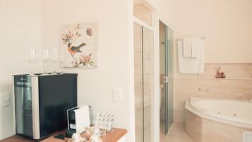 A modern bathroom with a large bathtub, a glass shower enclosure, and a wooden vanity with a coffee machine and glasses.