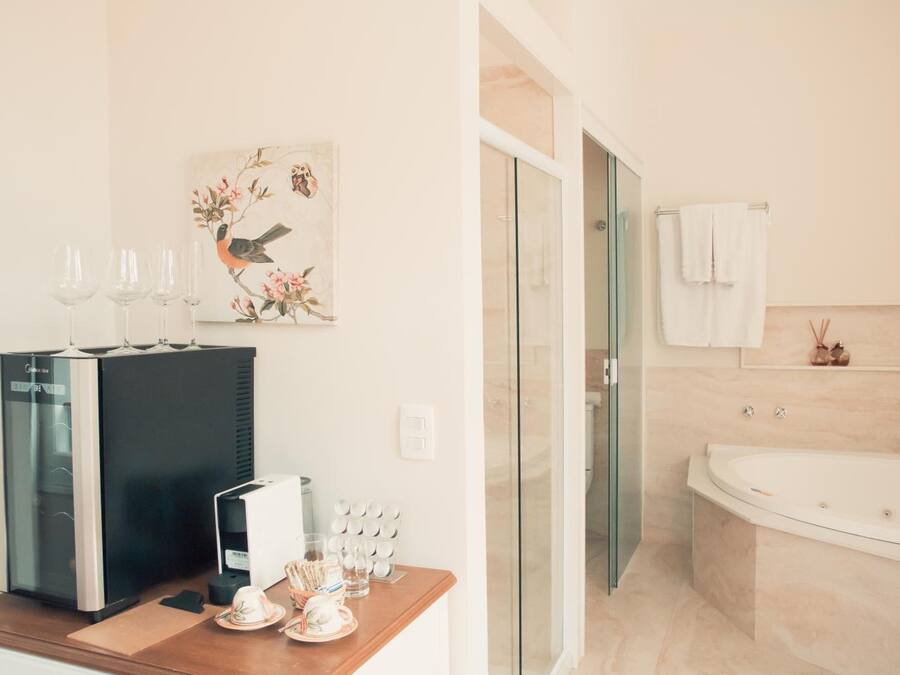 A modern bathroom with a large bathtub, a glass shower enclosure, and a wooden vanity with a coffee machine and glasses.