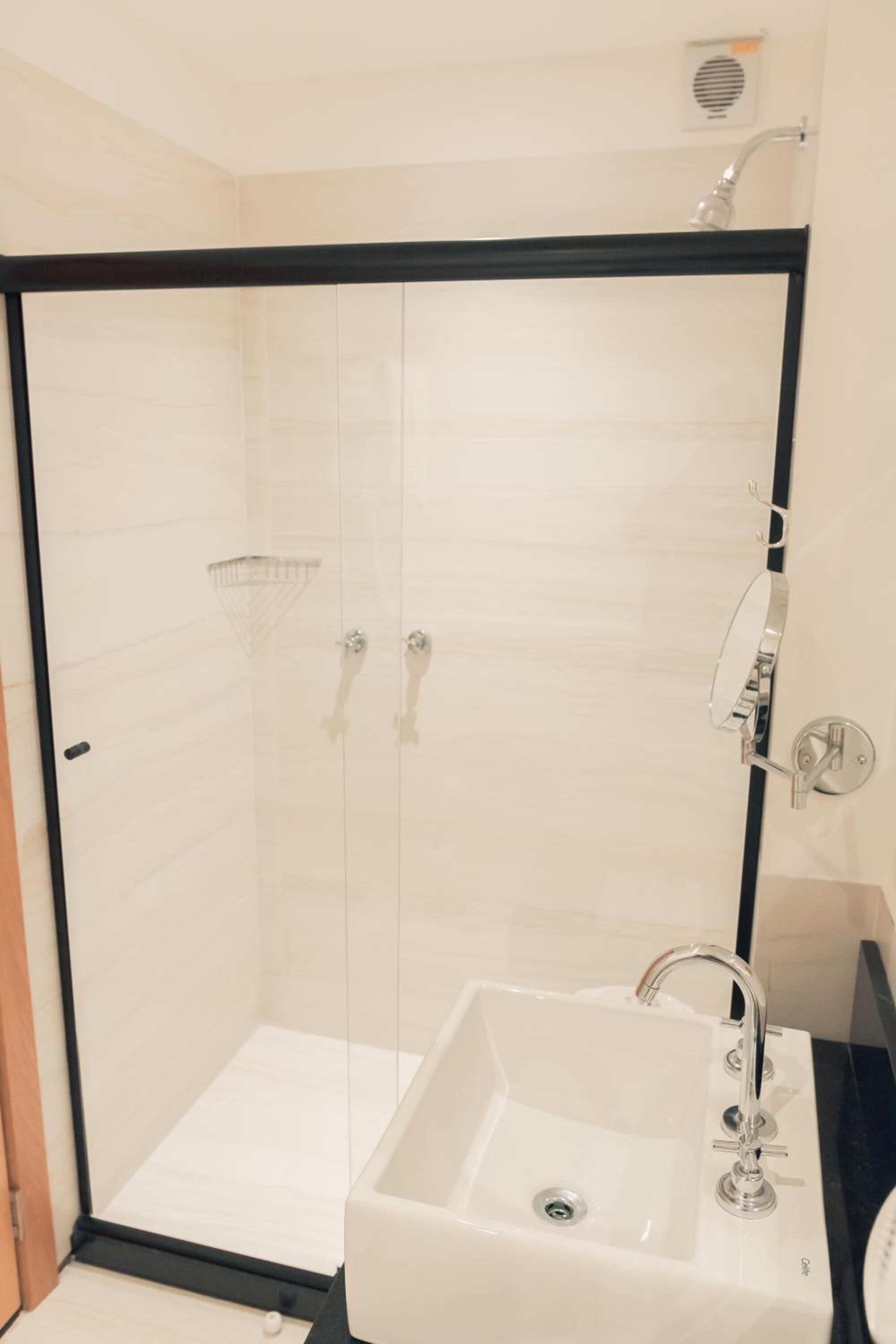 A modern bathroom with a glass-enclosed shower, a white sink, and a handheld showerhead.
