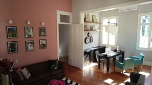 A living room with a sofa, a dining table with chairs, a staircase, and a wall with framed pictures. - Casa Rosa Hotel Boutique (Petrópolis)