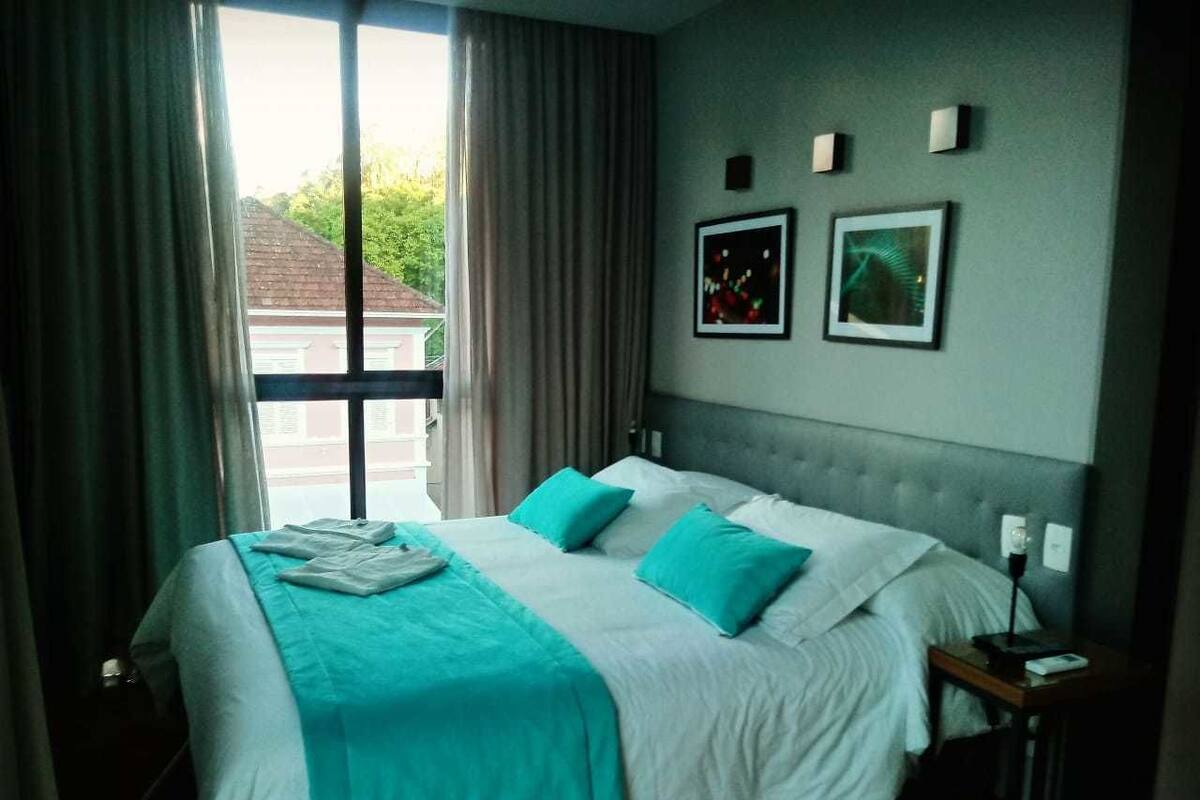 A hotel room with a large bed, two pillows, a nightstand, and a window with curtains.